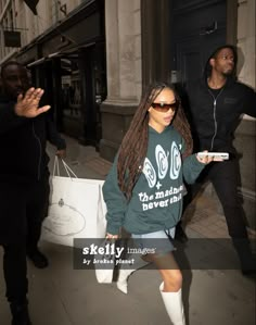 a woman is walking down the street with her handbag in her other hand and another man standing next to her