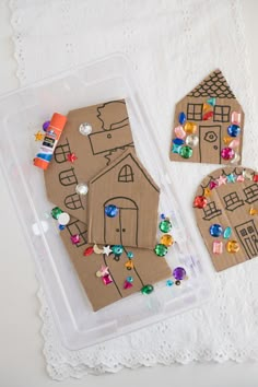 two cardboard houses are sitting on a doily next to some beads and other crafting supplies