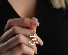 Discover inner peace with our Handmade Gold Aum Symbol Necklace, featuring a delicate pendant inspired by the sacred Om symbol. Meticulously crafted in two exceptional material options: 925 sterling silver and 14K solid gold, this necklace allows you to choose between classic elegance and the enduring warmth of gold. While the choice of materials is significant, the true essence lies in the profound symbolism of the Aum symbol. Whether you opt for the timeless allure of gold or the classic beauty of silver, this necklace is more than jewelry; it's a spiritual companion, a reminder of the universal sound that represents the essence of all creation. Each Aum Symbol Necklace is presented in an elegant gift box, ready to be shared on special occasions like birthdays, graduations, or any celebr Spiritual Round Pendant For Gift, Spiritual Pendant Necklaces As Gifts, Handmade Spiritual Necklaces For Gifts, Symbolic Necklaces For Festivals, Symbolic Pendant Charm Necklaces For Meditation, Spiritual Necklaces For Festivals And Gifts, Spiritual Necklaces For Gifts And Festivals, Spiritual Necklace For Festivals And Gifts, Spiritual Pendant Necklace