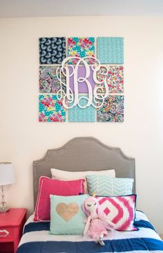 a bed topped with pillows and blankets next to a wall mounted monogrammed art