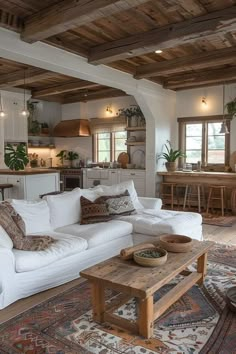 a living room filled with white furniture and lots of wood flooring next to a kitchen