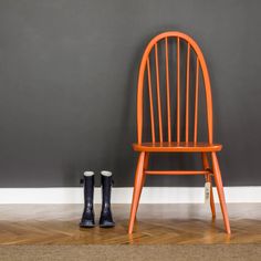 an orange chair and two black boots are on the floor in front of a gray wall