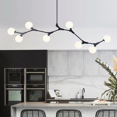 a modern kitchen with black chairs and white counter tops, lights hanging from the ceiling