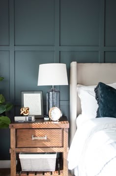 a bedroom with dark green walls and white linens on the bed, along with a wooden night stand