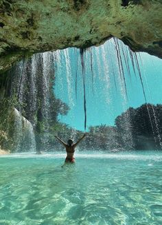 a person standing in the water under a waterfall with their arms up and hands out