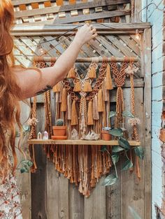 a woman is pointing at some tassels hanging on a rack outside in front of a wooden fence