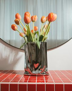 a vase filled with orange tulips sitting on top of a red tiled counter