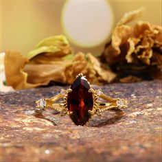 a red stone ring sitting on top of a rock next to dried flowers and leaves