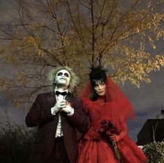 two people dressed up in costumes standing next to each other near a tree with leaves on it