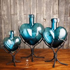 three blue glass vases sitting on top of metal stand next to a wooden wall