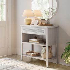 a white table with a mirror and lamp on it next to a plant in a room