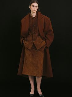 a woman standing in front of a black background wearing a brown coat and skirt with buttons