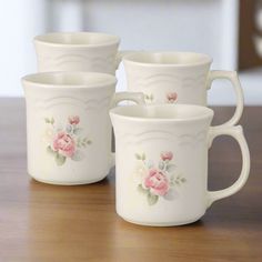 four white cups with pink flowers on them sitting on a wooden table top next to each other