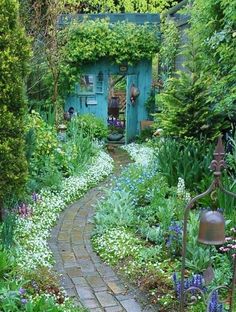 a garden with lots of green plants and flowers around the path leading to a blue door