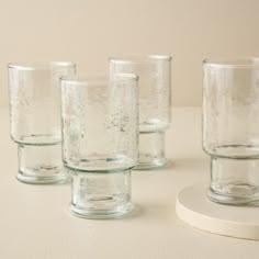 four clear glass cups sitting on top of a white table next to each other,