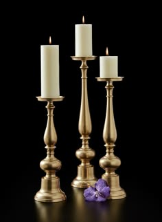 three brass candlesticks with one candle lit and the other turned on, in front of a black background