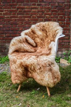 a chair made out of fur sitting in front of a brick wall with grass on the ground