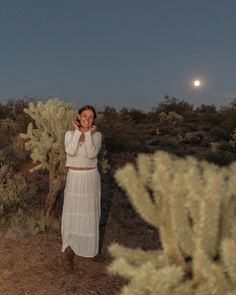 a woman is standing in the desert with her hands on her face and looking up at the sky