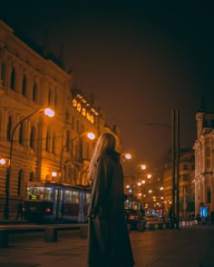 a woman standing in the middle of a street at night with her back to the camera