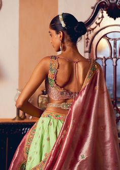 Embrace timeless elegance with this classic kalidar lehenga set, crafted from light green jacquard silk banarasi. Featuring intricate embroidery enhanced with zari and zardozi work, the design is further adorned with dabka, sequins, pearls, and gota texturing. The ensemble includes a heavily embroidered blouse made from pastel pink silk zari tissue, adorned with a floral embroidery pattern and embellished with pearl tassels. Complementing the set is a shimmering pastel pink silk zari tissue dupatta, featuring floral embroidered motifs and a patchwork embroidered border. A signature embellished belt creates a gracefully defined and sophisticated silhouette. Pista Green Tissue Silk Choli With Cutdana, Green Anarkali Choli In Tissue Silk, Reception Sharara With Unstitched Blouse In Banarasi Silk, Meenakari Raw Silk Pre-draped Saree For Wedding, Green Tissue Silk Lehenga For Wedding, Green Lehenga In Tissue Silk With Traditional Drape, Green Banarasi Silk Sharara For Wedding, Silk Lehenga With Meenakari Detailing, Brocade Meenakari Sets For Reception