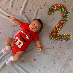 a baby laying on top of a bed covered in sprinkles next to the number two