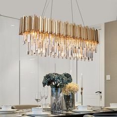 a chandelier hanging over a dining room table with plates and glasses on it