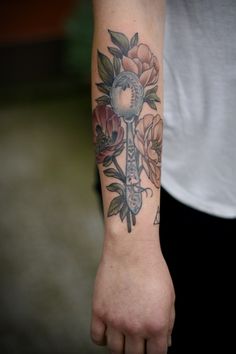 a person with a tattoo on their arm holding a key and flowers in the background