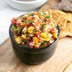 a black bowl filled with salsa next to crackers on a wooden cutting board,