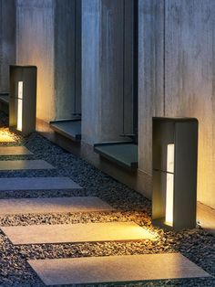 some lights that are on the side of a building near rocks and gravel flooring