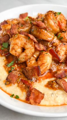 a white plate topped with grits covered in sauce and shrimp on top of it