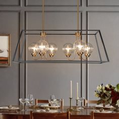 a chandelier hanging over a dining room table with place settings on the side