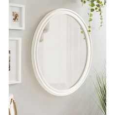 a white round mirror hanging on the wall next to a potted plant and framed pictures