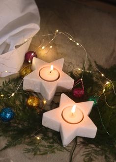 three white candles sitting on top of a table next to some christmas ornaments and lights