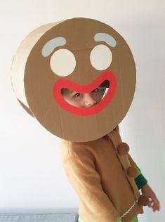 a young child wearing a cardboard face with a red nose and mouth ring on it's head