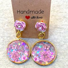 a pair of earrings with pink flowers and butterflies on the dangle, sitting in front of a card