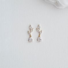 two pairs of diamond earrings sitting on top of a white cloth next to a flower