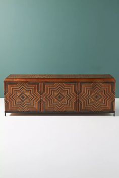 an art deco sideboard in wood with geometric designs on the front and sides, against a teal green wall