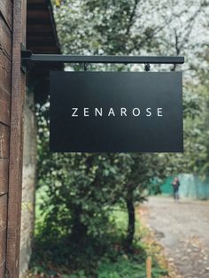 a black sign hanging from the side of a wooden building next to a sidewalk and trees