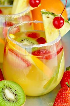 two glasses filled with fruit and garnish on top of a table next to oranges