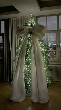 a white christmas tree with lights in front of it and a large bow on the top