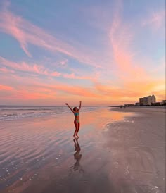 a woman standing on the beach with her arms up in the air as the sun sets