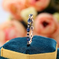 a close up of a ring on top of a blue velvet box with flowers in the background