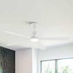 a white ceiling fan mounted on the side of a wall in a room with large windows