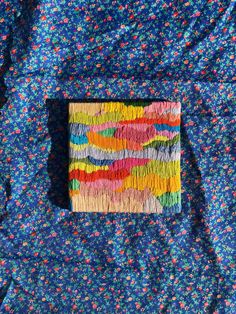 a piece of art made out of yarn on top of a blue cloth covered in multicolored flowers