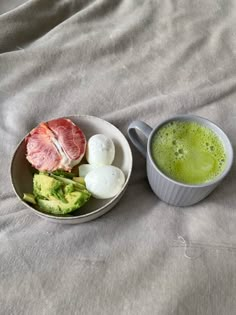 a bowl of food and a cup of green liquid on a bed