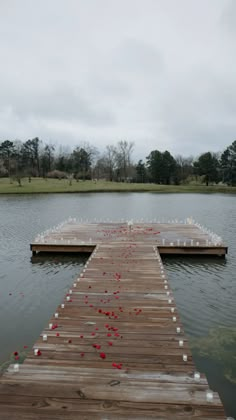 a wooden dock with candles on it in the middle of a lake surrounded by grass and trees