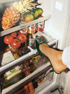 a woman's feet in front of an open refrigerator filled with fruit and vegetables