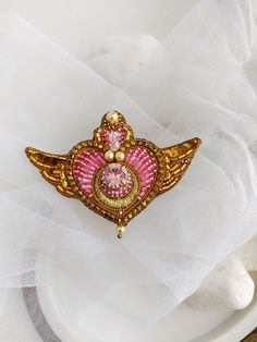 a pink and gold brooch sitting on top of a white cloth covered tablecloth