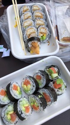 two trays filled with sushi and chopsticks on top of a table