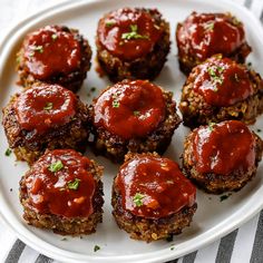 small meat patties covered in marinara sauce on a white plate with a striped napkin